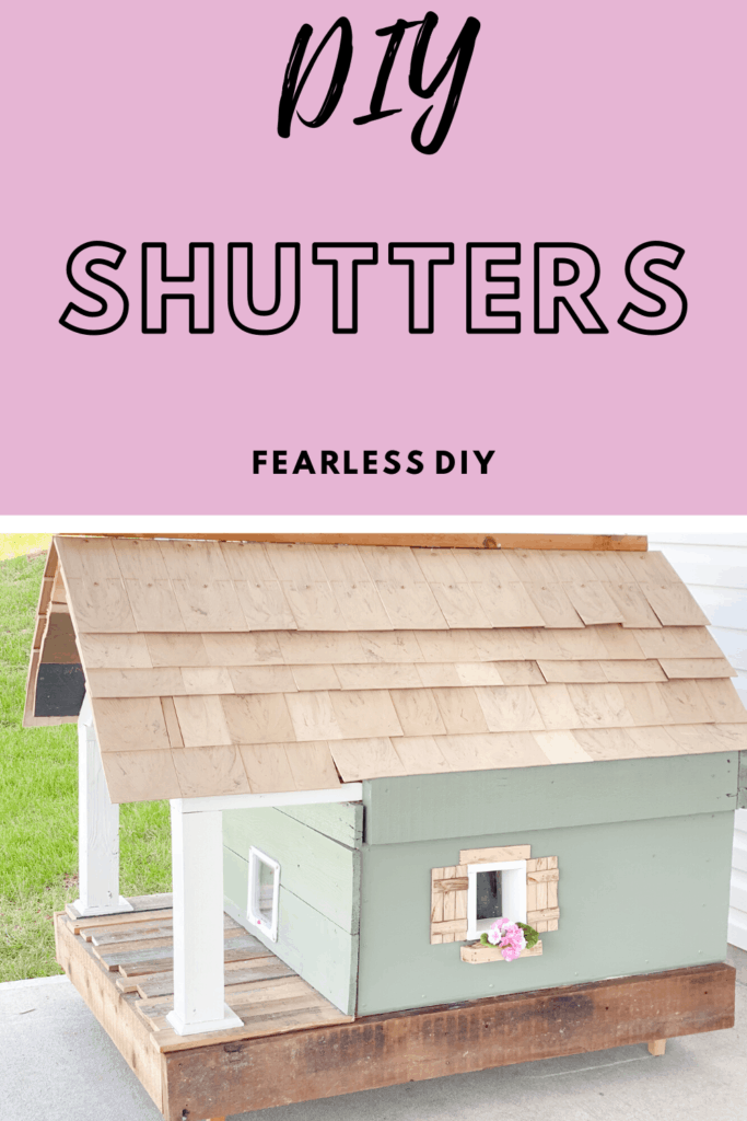 Craftsman style cat house painted green with cedar shakes, white front porch columns and oak shutters and flowerbox with pink flowers