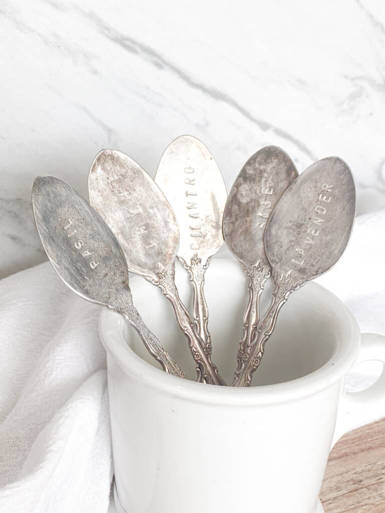 antique stamped spoons in a white ironstone mug in front of a marble backpslash