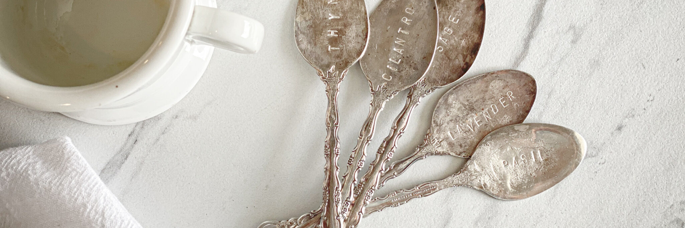 stamped antique spoons next to ironstone mug, flour sack towel and marble