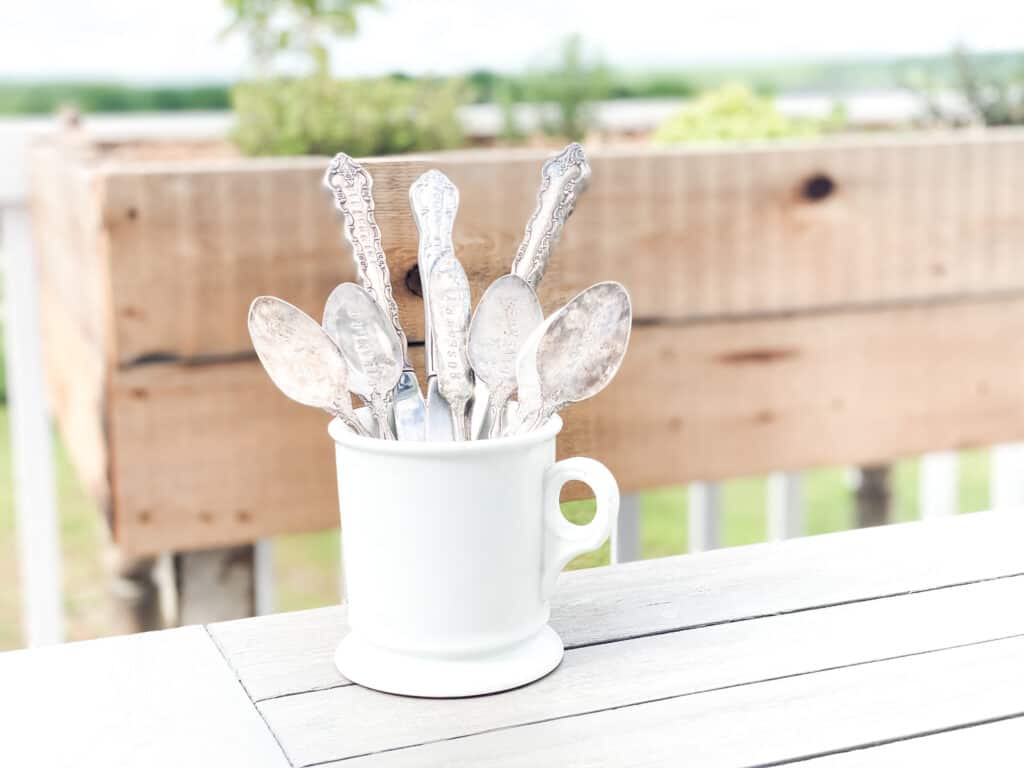 stamped antique herb markers in white ironstone mug in front of a reclaimed wood raised herb garden