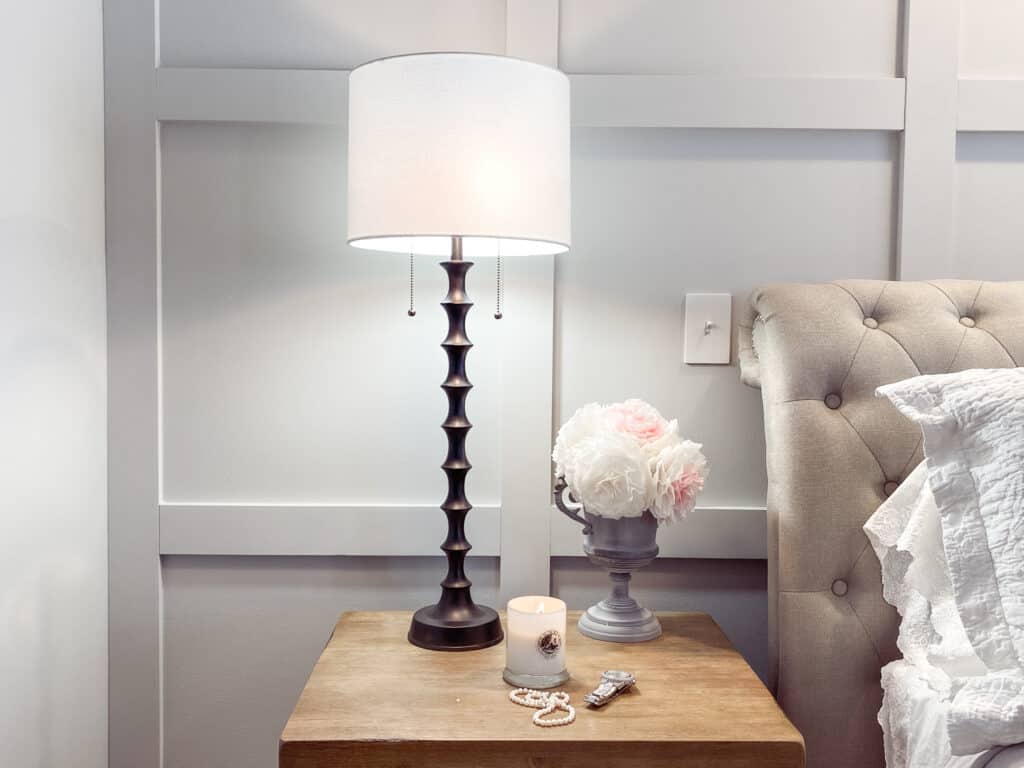 board and batten master bedroom wall with black lamp on natural wood nightstand with a string of pearls, watch and candle