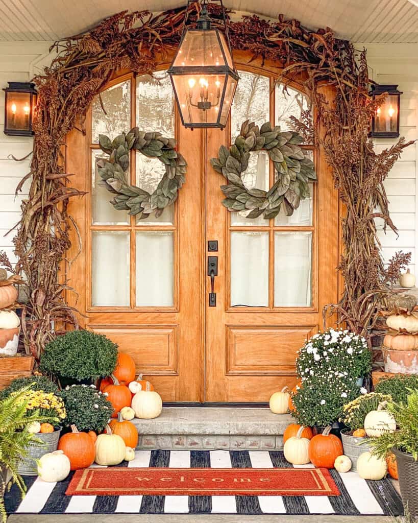 Pumpkins mums and black and white striped rug in front of arched wooden doors.