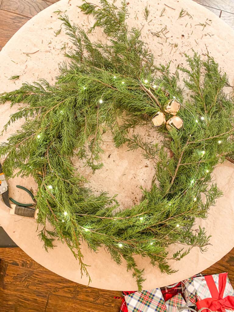 finished evergreen wreath with brass bells and lights lying on a table with plaid wrapped Christmas presents just visible