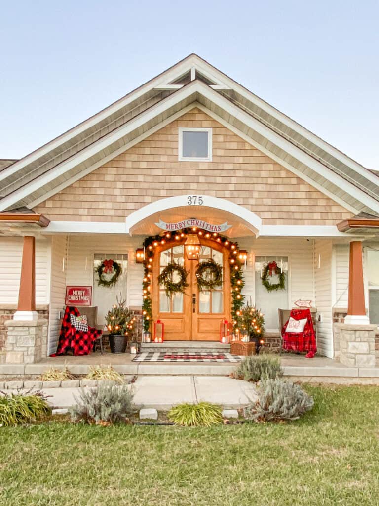 Christmas front porch with greenery with lights, red blankets and lanterns