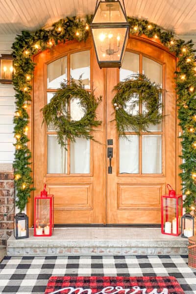 winter greenery around a wooden front door with lights entwined and lanterns