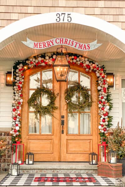 winter greenery around a wooden front door with lights entwined and lanterns